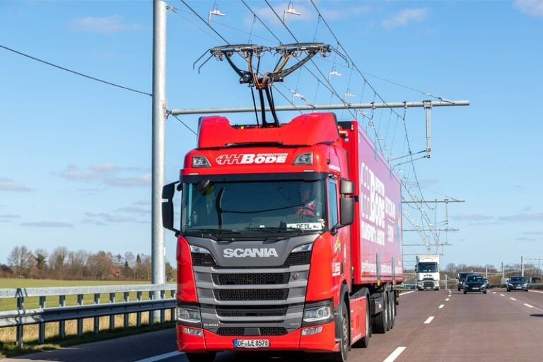 Czerwony ciężarówka Scania na drodze z przewodami elektrycznymi