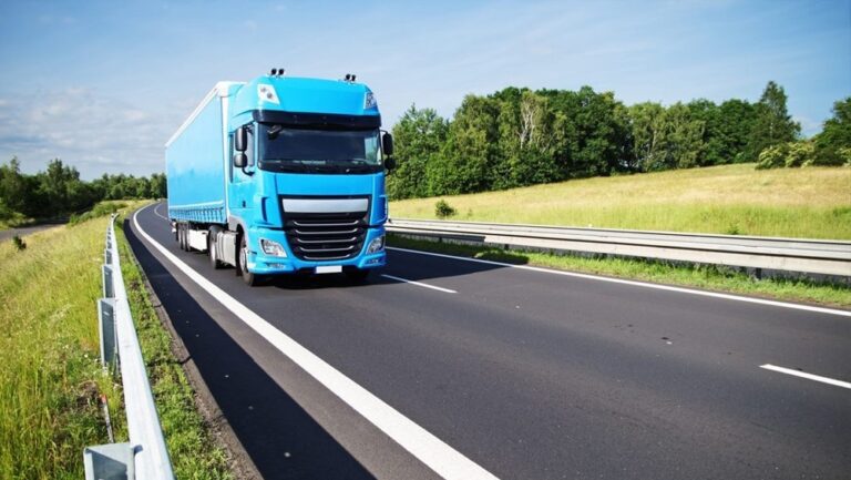 Niebieska ciężarówka na drodze w otoczeniu zieleni