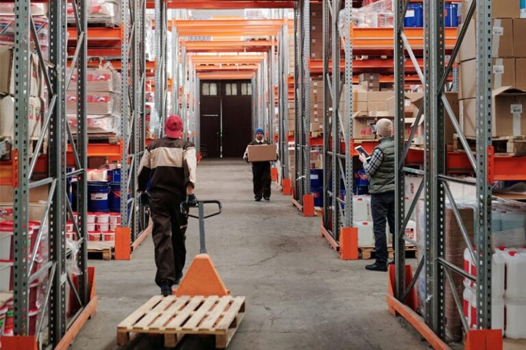 Magazynierzy pracują w magazynie z regałami.