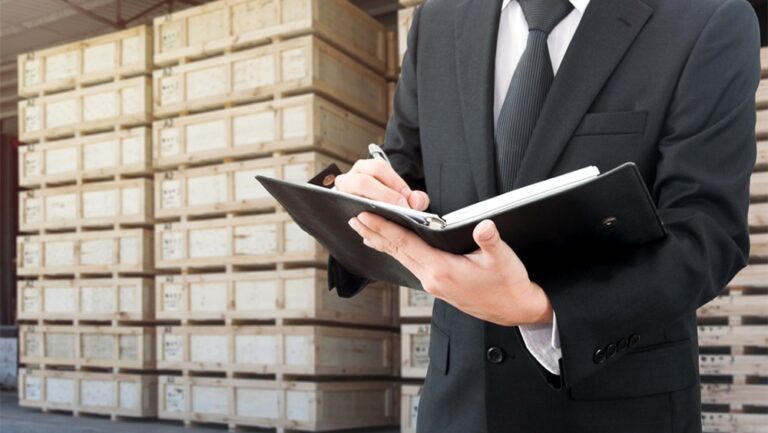 Mężczyzna w garniturze piszący w notatniku przed skrzyniami.