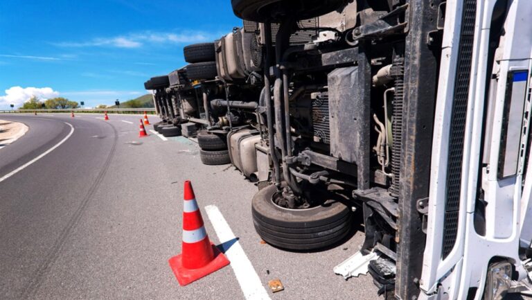 Przewrócony ciężarówka na drodze z pachołkami.
